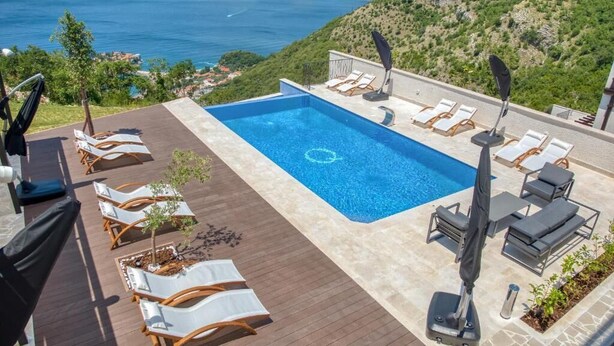 Ein Pool auf dem Dach mit Liegestühlen und Blick auf das Meer und die Berge.