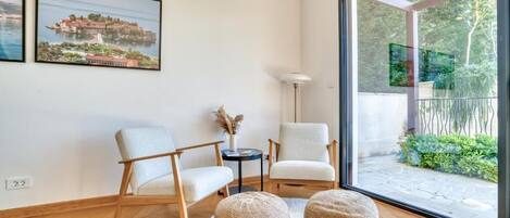 A modern living room with two chairs, a round rug, and a large window with a view of greenery.