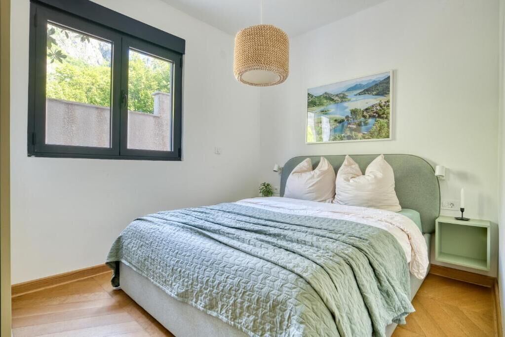 Een slaapkamer met een bed, een raam, een schilderij en een nachtkastje.