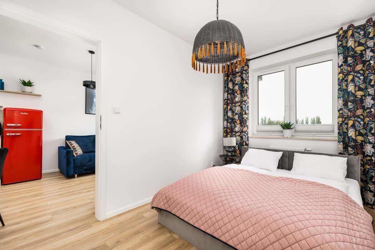 Ein modernes Schlafzimmer mit einem großen Bett, einem roten Kleiderschrank, einem blauen Sofa und einem Fenster mit Vorhängen.