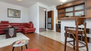 Een woonkamer met een rode bank, een kleine tafel en een houten stoel. Er is een keuken met houten kasten en een eettafel.
