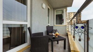 Een balkon met rieten meubels, een tafeltje met een vaas en een decoratieve metalen balustrade.
