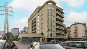 Een meerhoog woongebouw met balkons, een parkeersbord en een elektriciteitspylon in de achtergrond.