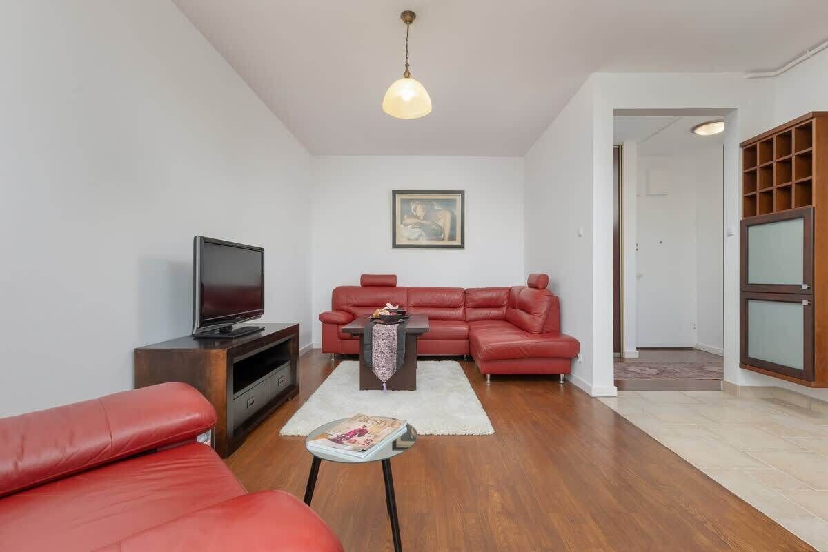 A spacious living room with red leather sofas, a coffee table, and a TV on a wooden stand.
