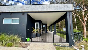 Un edificio moderno con fachada oscura, un acceso cubierto y un camino de entrada con portón.