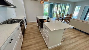 Una cocina moderna con muebles blancos, una isla central y un comedor con sillas de madera.