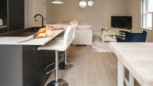 A modern kitchen with a central island, bar stools, a dining table, a sofa, and a TV. - 3 Compass Point (Weymouth)