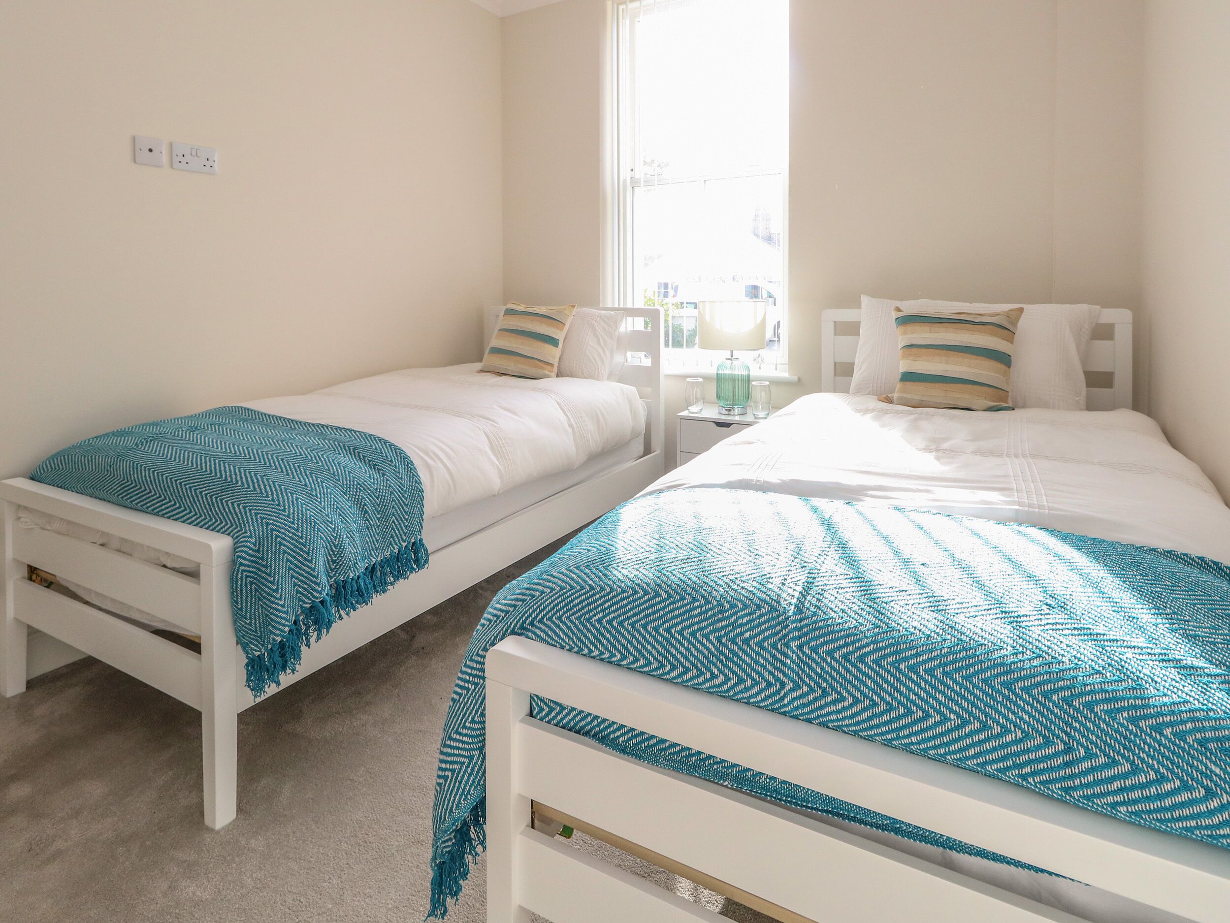 Une chambre avec deux lits simples, une table de chevet, une lampe et une fenêtre donnant sur des immeubles.