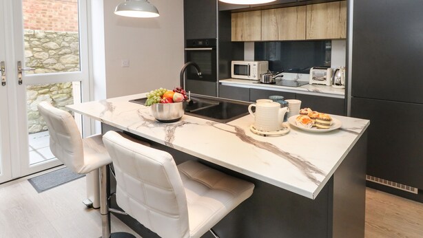 A modern kitchen with a marble countertop, a built-in microwave, and a sink. - 3 Compass Point (Weymouth)