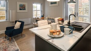 A modern kitchen with a marble countertop, a sink, and a dining area with a table and chairs. - 3 Compass Point (Weymouth)