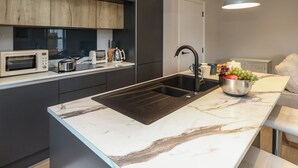A modern kitchen with a marble countertop, a black sink, and a microwave. - 3 Compass Point (Weymouth)