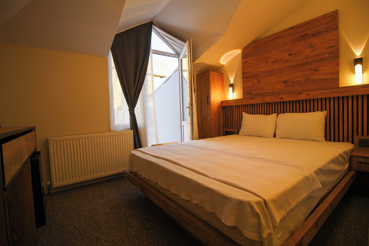 A bedroom with a wooden headboard, a large bed with white bedding, a radiator, and a window with curtains.