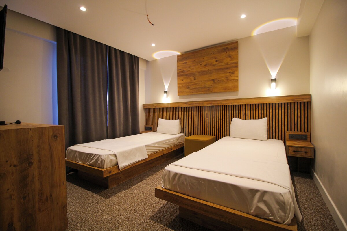 A hotel room with two single beds, a wooden headboard, a desk, and a wall-mounted light fixture.