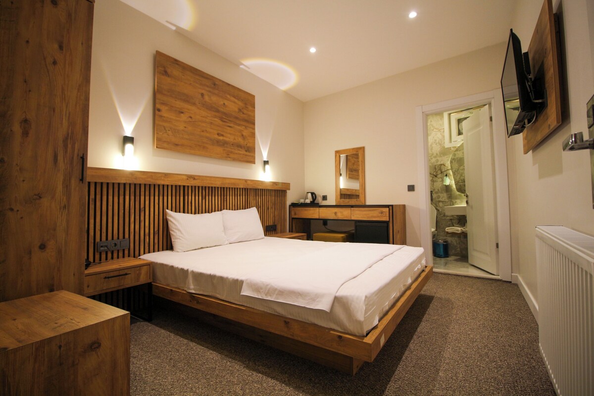 A bedroom with a wooden bed, bedside tables, a nightstand, a mirror, and a television on the wall.