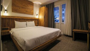 Ein modernes Hotelzimmer mit einem Holzkopfteil, einem großen Bett, einem Nachttisch, einem Kleiderschrank und Blick ins Freie.