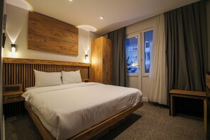 A modern hotel room with a wooden headboard, a large bed, a nightstand, a wardrobe, and a view of the outside. - Luvira Hotel  (Istanbul)