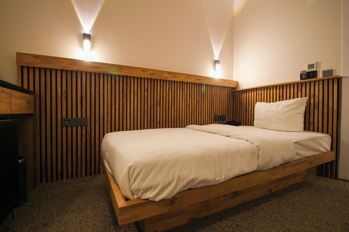 A wooden bed with a headboard, two wall-mounted light fixtures, and a small shelf with items.