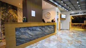 Ein Hotel-Empfangsbereich mit Marmor-Theke, einer Uhr und Schildern für Frühstück und Kinderbetreuung.
