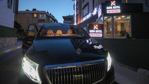 Ein schwarzes Auto vor einem Gebäude mit der Aufschrift 'Kawa Hotel Eingang'.