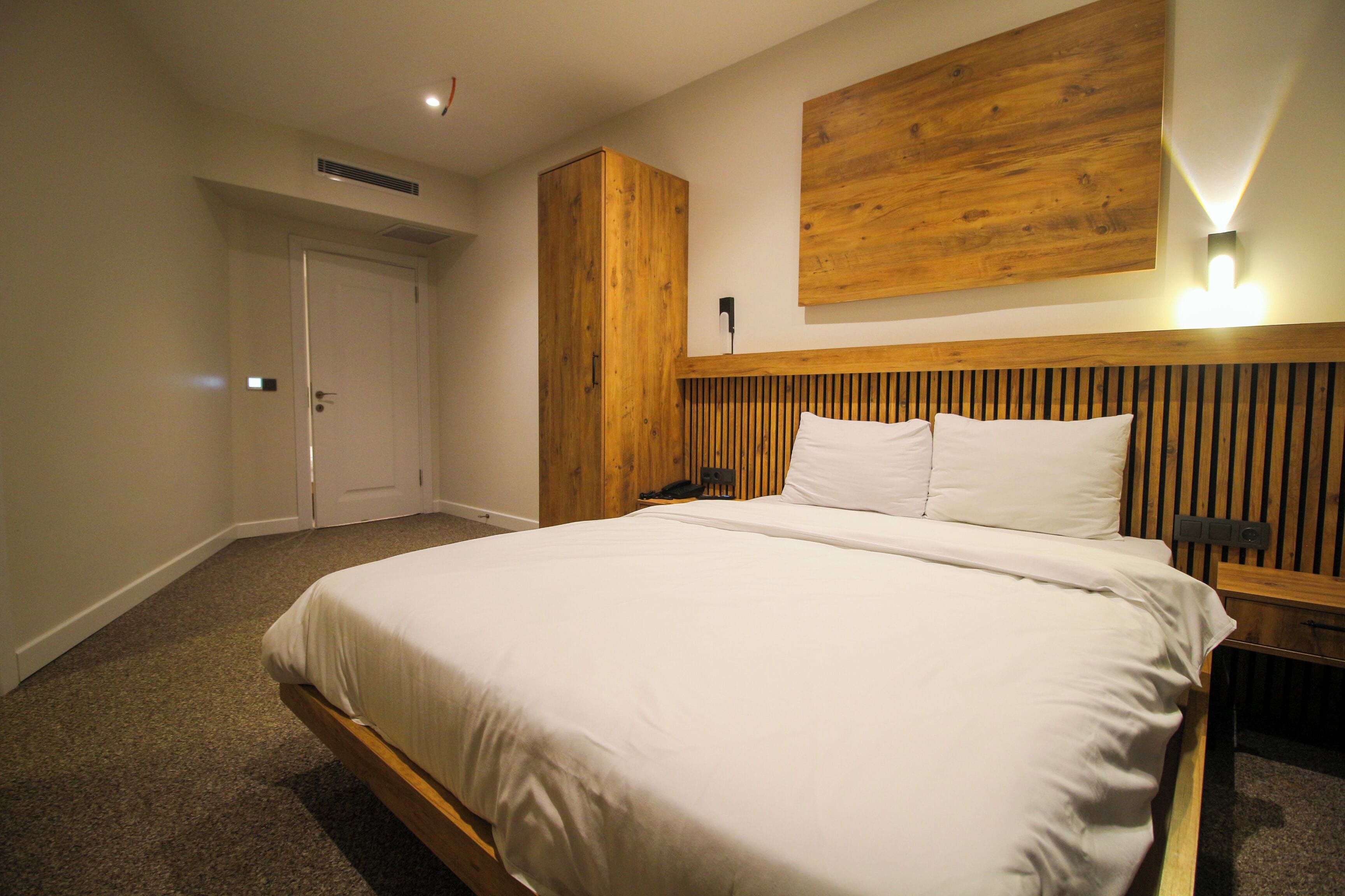 A bedroom with a large bed, wooden headboard, a wall-mounted light, and a door.