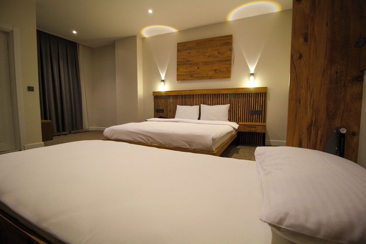 A hotel room with two beds, wooden headboard, and wall-mounted lighting.
