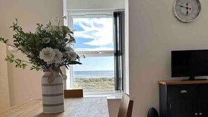 A dining area with a table, chairs, a vase with flowers, a TV, and a clock on the wall. - Remarkable 1-bed Seaview Beach Apartment Barmouth (Barmouth)