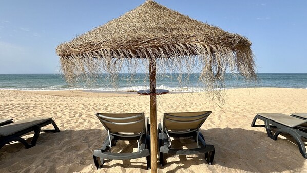 A beach umbrella with a woven structure, two beach chairs, and a table with a round top.