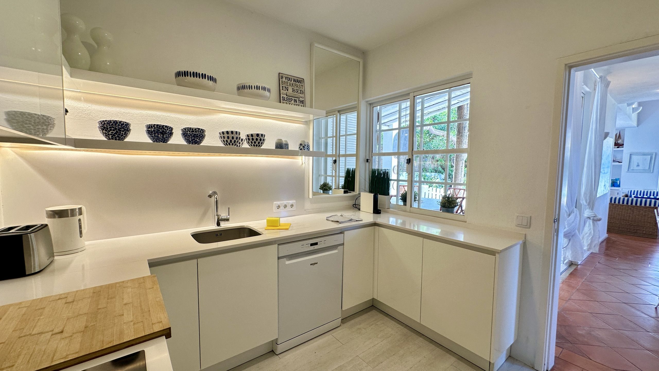 A modern kitchen with white cabinetry, a built-in dishwasher, and a window providing natural light.