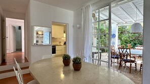 A modern kitchen with white cabinets, a dining area with a table and chairs, and a view of the outdoors through large windows.