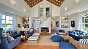 A spacious living room with a high ceiling, a fireplace, and a staircase leading to an upper level.