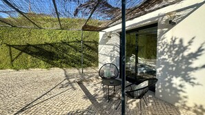 A patio with a table and chairs, a glass door, and a hedge in the background. - Strip by Check-in Portugal (Albufeira)
