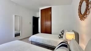 A bedroom with two beds, a wooden wardrobe, a mirror, and a bedside lamp. - Strip by Check-in Portugal (Albufeira)