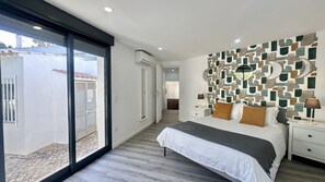 A modern bedroom with a large bed, a nightstand, a wall with geometric patterns, and a sliding glass door leading to a balcony. - Strip by Check-in Portugal (Albufeira)