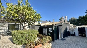 A building with a tiled roof, a black door with a circular window, and a small garden area with a tree and shrubs. - Strip by Check-in Portugal (Albufeira)