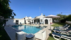 A swimming pool with lounge chairs and umbrellas, surrounded by a building with a tiled roof. - Strip by Check-in Portugal (Albufeira)