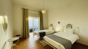Un dormitorio con dos camas, una mesita pequeña y un balcón con cortinas.