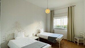 Una habitación con dos camas, una ventana con cortinas, una silla y una lámpara colgante.