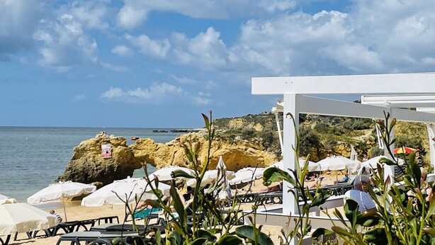 Une vue sur la plage, avec des formations rocheuses, une pergola blanche et des parasols de plage.