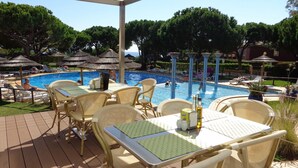 Un espace aménagé au bord de la piscine, avec des fauteuils et des tables en osier, une piscine et des parasols.