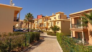 Une rue résidentielle bordée d’immeubles à plusieurs étages, avec un chemin pavé et des voitures garées.
