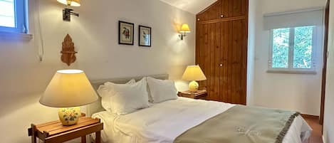 Un dormitorio con cama, dos lámparas de noche, un armario de madera y una ventana con vistas a zonas verdes.