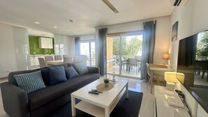 Un salon moderne comprenant un canapé, une table basse, un téléviseur et un balcon aménagé avec du mobilier d’extérieur.