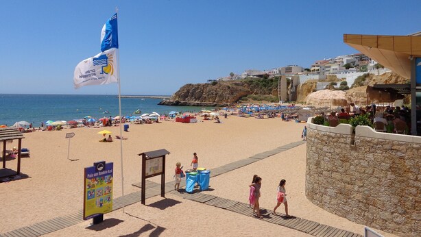Une plage avec un drapeau, des parasols et un panneau indicateur.