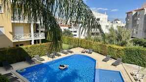 Une piscine avec des chaises longues, une personne sur un flotteur et un bâtiment doté de balcons.