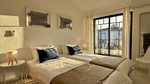 Quarto de hotel com duas camas, uma janela grande e obras de arte nas paredes.