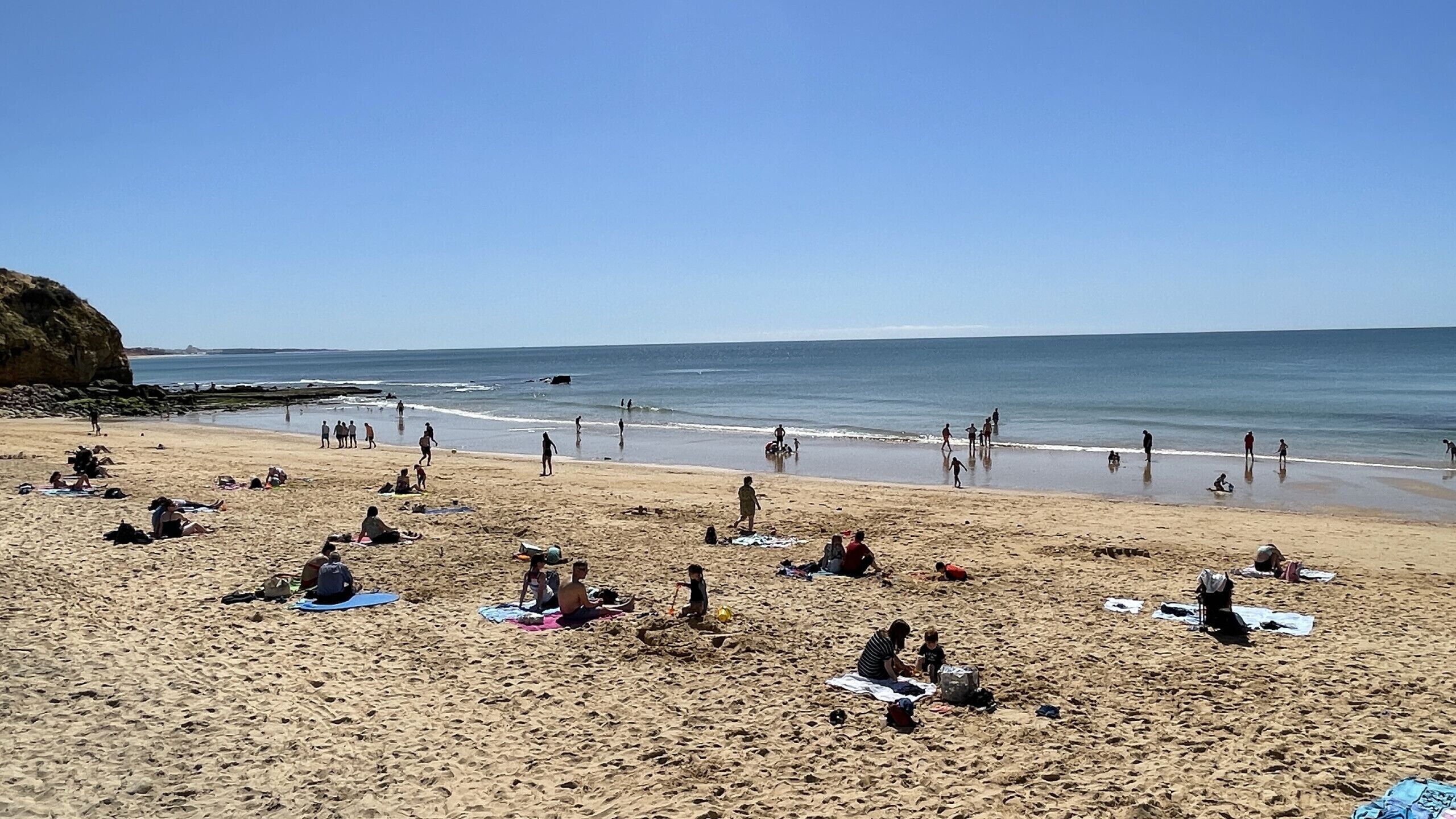 A beach with people sunbathing and swimming.