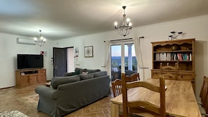A living room with a sofa, TV, wooden cabinet, dining table, chairs, and a bookshelf.