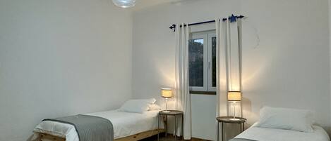 A room with two single beds, a window with curtains, two bedside lamps, and a green rug.