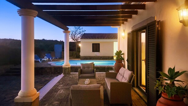 A covered outdoor area with a pool, lounge chairs, and a seating arrangement.