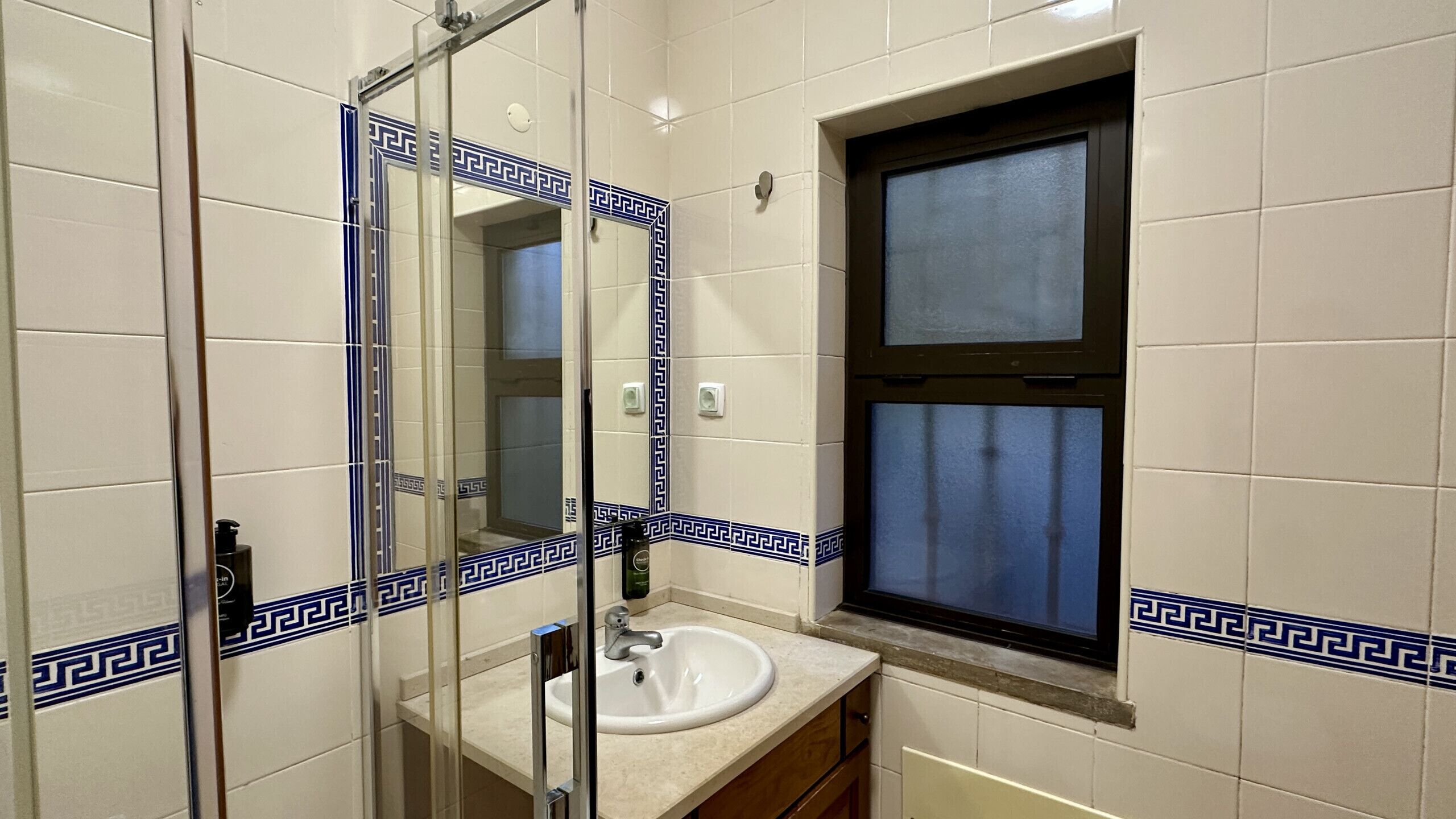 A bathroom with a white sink, a mirror, and a window with a blue curtain.